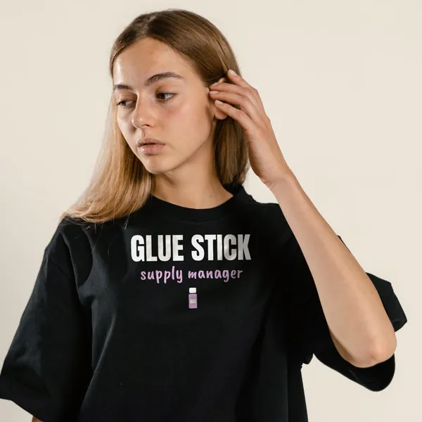 Model wearing a black "Glue Stick Supply Manager" tee with the light-ink version of the design