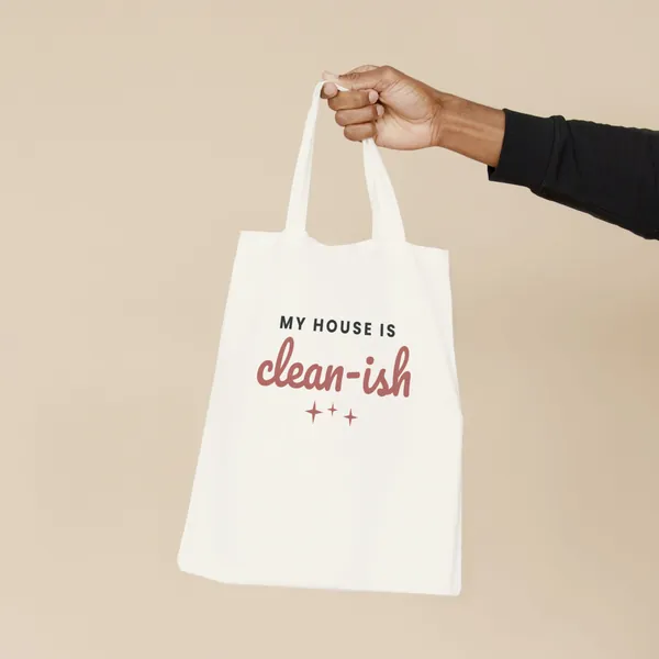 Natural canvas tote bag printed with "My House Is Clean-ish", held by the handles
